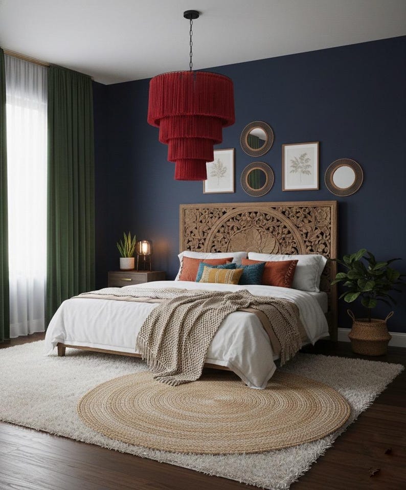 May include: A bedroom featuring a large carved wooden headboard, a white bedspread with a beige knit throw, and a tiered red fringe pendant light. The room includes a round jute rug, dark blue walls, green curtains, and framed wall art.