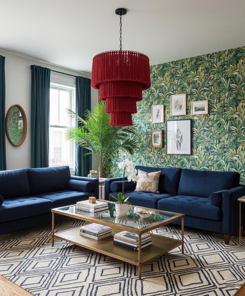 May include: A tiered red fringe chandelier hangs above a rectangular glass-top coffee table with a gold metal frame. Two navy blue sofas are positioned on a cream and black geometric rug in front of a wall with green tropical leaf wallpaper.