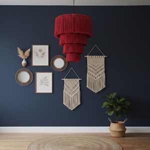 May include: A tiered, deep red fringe chandelier hangs from a black ceiling mount. The fixture features four concentric circular layers of red yarn, creating a cascading, cylindrical shape that provides a bold focal point in the room.