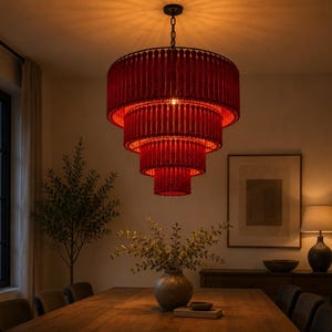 May include: A tiered chandelier featuring four concentric circular layers of deep red fringe. The fixture is suspended by a dark metal chain and emits a warm, glowing light that illuminates the surrounding space from within the layered fabric.