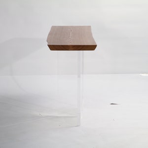 Puede incluir: Una mesa consola de madera con una tapa de borde vivo y patas de acr&iacute;lico transparente. La mesa est&aacute; hecha de madera natural con un acabado marr&oacute;n claro.