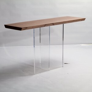 Puede incluir: Una mesa consola moderna con una tapa de madera natural y patas de acr&iacute;lico transparente. La mesa tiene un dise&ntilde;o simple y minimalista y ser&iacute;a una gran adici&oacute;n a cualquier sala de estar o entrada.