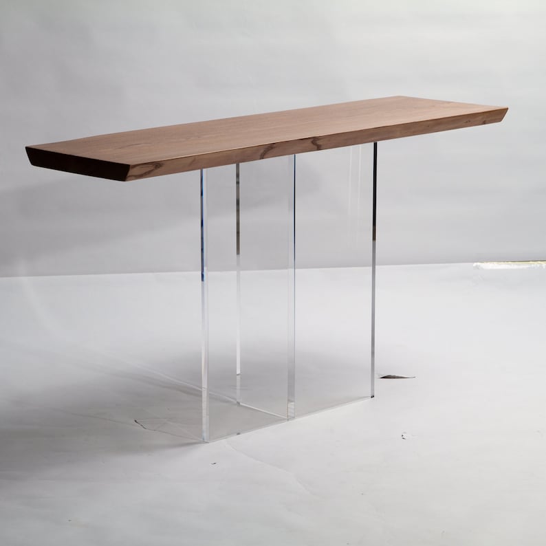 Puede incluir: Una mesa consola moderna con una tapa de madera natural y patas de acr&iacute;lico transparente. La mesa tiene un dise&ntilde;o simple y minimalista y ser&iacute;a una gran adici&oacute;n a cualquier sala de estar o entrada.