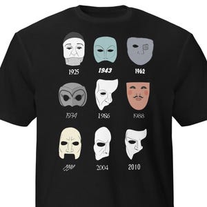 May include: Black t-shirt featuring a graphic of nine different theatrical masks, each with a year below it. The masks are in various colors and styles, including a full face, half-masks, and eye masks. The years range from 1925 to 2010.