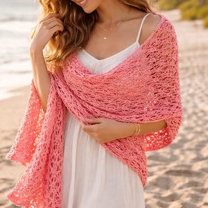 Może przedstawiać: Koralowa, ażurowa chusta narzucona na białą sukienkę. Chusta ma delikatny, ażurowy wzór i jest noszona na plaży. Chusta wykonana jest z miękkiego, lekkiego materiału.