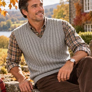 May include: A light gray V-neck sweater vest with a vertical ribbed knit pattern worn over a long-sleeved plaid button-down shirt in shades of brown, tan, and blue, paired with dark brown corduroy trousers and a wristwatch with a brown leather strap.