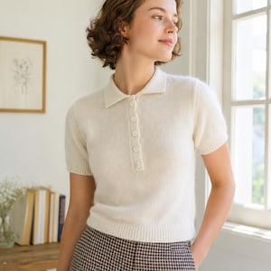 Peut inclure: Un polo en tricot crème à manches courtes doté d'un col classique, d'une patte de boutonnage avec cinq boutons assortis, ainsi que de finitions côtelées aux poignets et à la base, réalisé dans une maille douce et texturée.