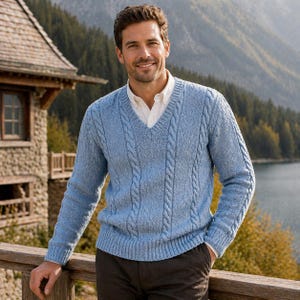 Könnte beinhalten: Hellblauer Zopfstrickpullover mit V-Ausschnitt. Der Pullover hat ein strukturiertes Design und wird über einem weißen Hemd mit Kragen getragen. Die Person steht im Freien in der Nähe eines Holzgeländers, mit einem See und Bergen im Hintergrund.