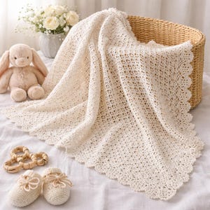 May include: A cream-colored crocheted blanket with an intricate openwork pattern and a scalloped edge, accompanied by a pair of matching crocheted booties, a set of wooden rings, and a plush tan rabbit toy tucked into a woven wicker basket.