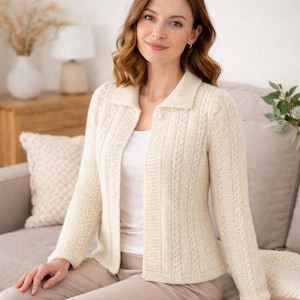 Può includere: Un cardigan in maglia color crema con colletto classico, maniche lunghe e dettagli a treccia verticali. Il capo è indossato sopra un top bianco semplice e abbinato a pantaloni chiari, mettendo in risalto la consistenza del tessuto lavorato.