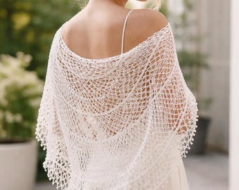 May include: A white crochet shawl featuring an intricate openwork pattern with a delicate scalloped edge and small bead-like accents along the hem. The lightweight garment drapes over the shoulders, showcasing a fine, airy texture and design.