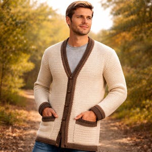 May include: A cream-coloured long-sleeve cardigan featuring a dark brown V-neck trim, matching dark brown sleeve cuffs, and two front pockets with dark brown edges. The garment is secured with a vertical row of small, dark brown buttons down the centre.