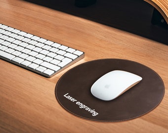 Pode incluir: Um mousepad de couro marrom com um mouse branco em cima. O mousepad tem o texto "Laser engraving".