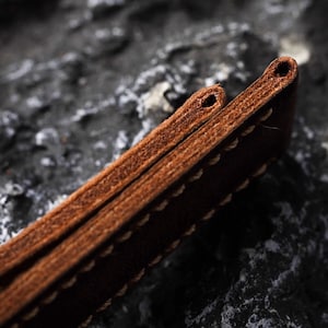 May include: Close-up of a brown leather watch strap with stitching. The strap is folded in half, showing the stitching detail.