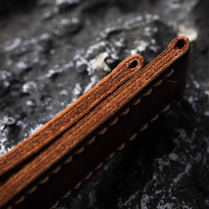 May include: Close-up of a brown leather watch strap with stitching. The strap is folded in half, showing the stitching detail.