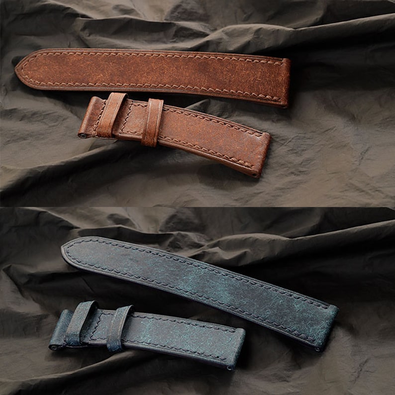 Op de afbeelding: Twee leren horlogebandjes. E&eacute;n is bruin met een verweerde afwerking en zichtbare stiksels. De andere is blauw met een verweerde afwerking en zichtbare stiksels. Beide bandjes hebben een gesp en worden gepresenteerd op een donkere, getextureerde ondergrond.
