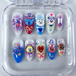 Pode incluir: Um conjunto de dez unhas postiças em formato amêndoa dentro de um estojo de plástico transparente. Cada unha apresenta um design único com gradientes coloridos, enfeites 3D, laços pintados à mão, estrelas, notas musicais e o logo BTS.