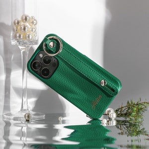 May include: A green leather phone case with a wrist strap and a gold ring. The case has the name "Helen" embossed on it.