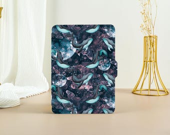 May include: A dark blue and purple phone case with a pattern of white whales swimming in a galaxy-like background.