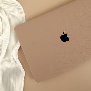 May include: A light brown laptop computer case with a black Apple logo. The case has a textured surface.
