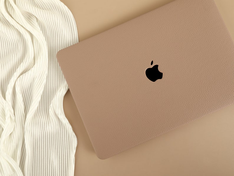 May include: A light brown laptop computer case with a black Apple logo. The case has a textured surface.