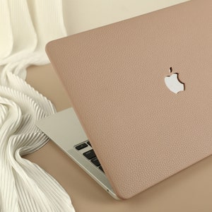 May include: A light brown leather laptop case with a white Apple logo. The case is closed and the laptop is visible underneath.