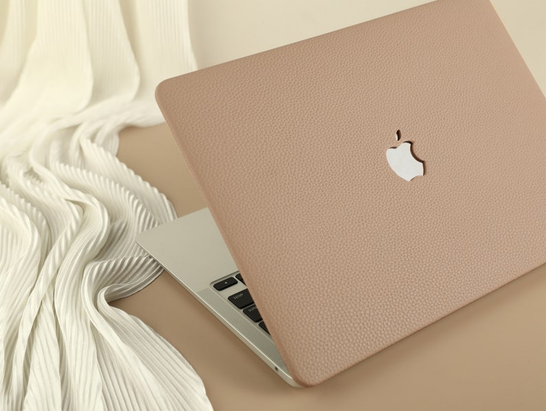 May include: A light brown leather laptop case with a white Apple logo. The case is closed and the laptop is visible underneath.