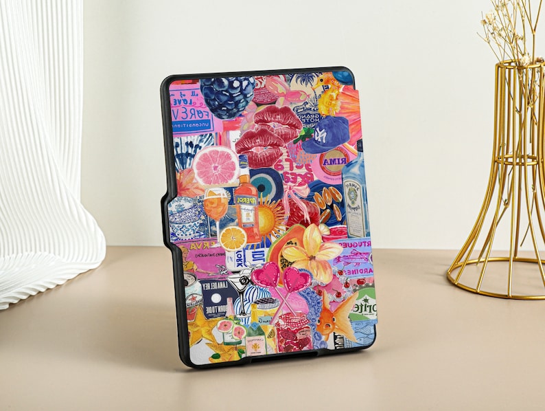 May include: A black e-reader case with a colorful collage design. The design includes images of fruit, flowers, hearts, and other objects. The text on the case includes the words 'FOREVER', 'RIMA', 'GIN', and 'GARDINE'. 