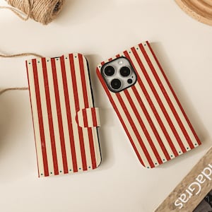 Peut inclure: Deux coques de téléphone à rayures verticales rouges et crème. L'une est de type portefeuille avec fermeture magnétique, l'autre est une coque arrière standard. Les coques sont posées sur une surface blanche.