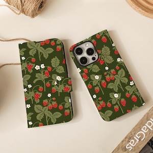 May include: Two phone cases featuring a strawberry pattern. The cases are dark green with a design of red strawberries, white flowers, and green leaves. One case is open, and the other is closed, showing the phone's screen.