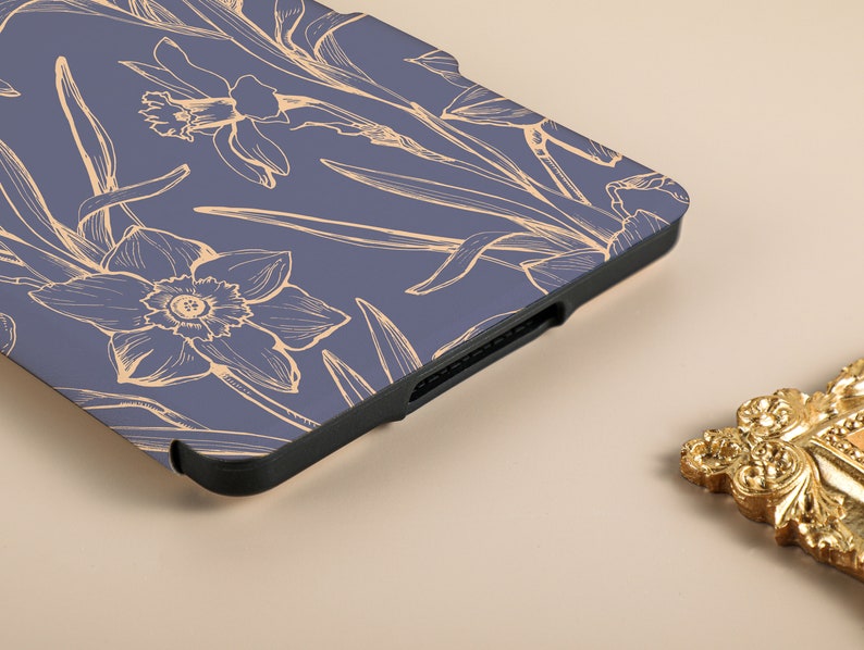 May include: A blue e-reader case with a floral design. The case has a black edge and a pattern of white daffodils on a blue background.