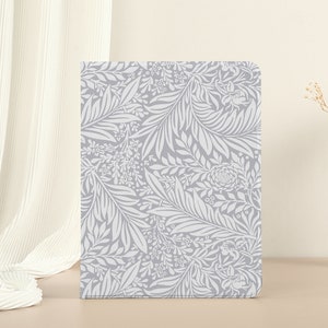 Op de afbeelding: Een grijze en witte notebookhoes met een bloemenpatroon. De hoes heeft een delicaat ontwerp van bladeren en bloemen.