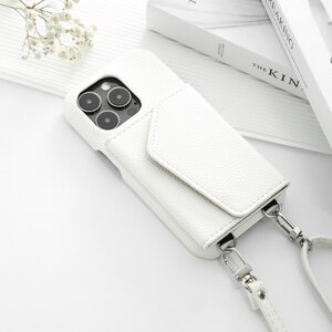 May include: White leather phone case with a flap and a white strap. The case has a camera lens cutout and a silver metal clasp.
