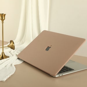 May include: A light brown leather laptop case with the Apple logo on the front. The case is closed and the laptop is visible underneath.
