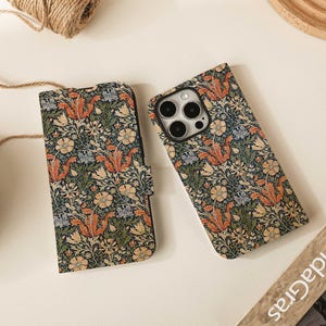 Op de afbeelding: Twee telefoonhoesjes met een bloemenpatroon in tinten oranje, blauw, groen en crème. Eén hoesje is open en onthult de camera van de telefoon. Het andere hoesje is gesloten. De hoesjes liggen op een lichtgekleurd oppervlak.