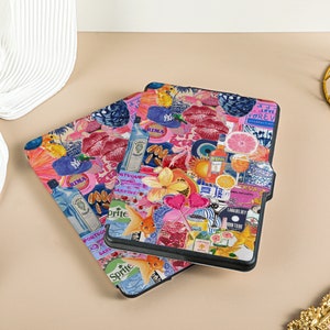May include: Two black e-reader cases with a colorful collage design. The design features pink lips, a blue eye, a pineapple, a papaya, a lime, a grapefruit, a gin bottle, a Sprite can, a fish, and the words 'Rima', 'Love Forever', 'Lanai', 'Don't Stop', 'Vogue', 'Gardine', and 'Cava'. 