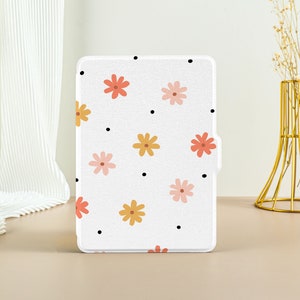以下が含まれることがあります： 白い電子書籍リーダーケースに花柄がプリントされています。花はピンク、オレンジ、イエローで、白い背景に黒いドットが散りばめられています。