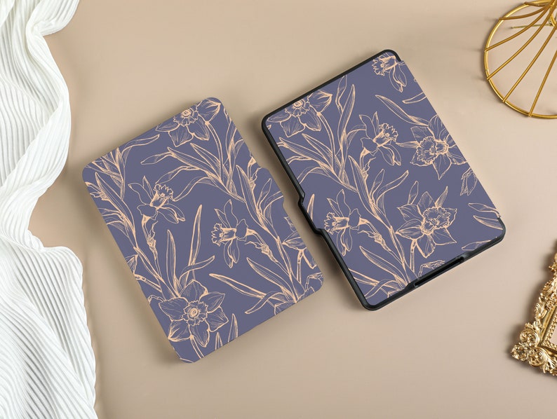 May include: Two purple e-reader cases with a floral design. The design features delicate, light orange daffodils and leaves on a dark purple background.