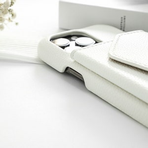 May include: White leather phone case with a flap that folds over the camera lens. The case has a textured surface.