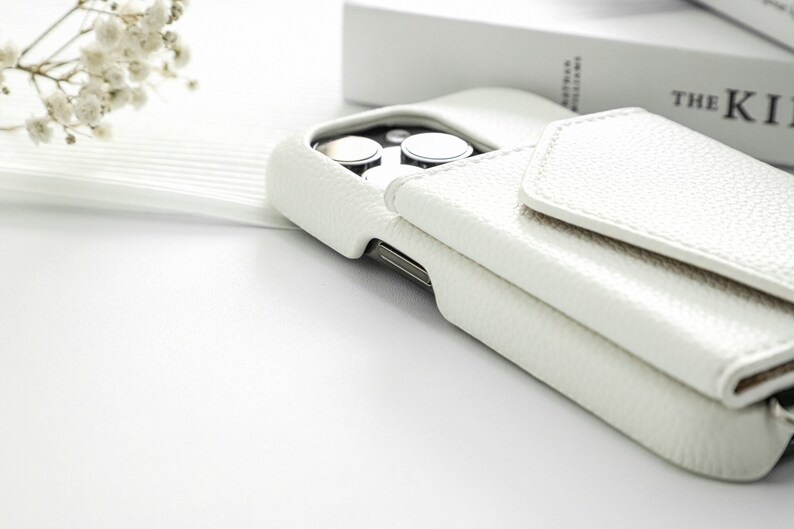 May include: White leather phone case with a flap that folds over the camera lens. The case has a textured surface.