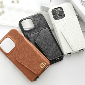 May include: Three phone cases with a pocket on the back. The cases are brown, black, and white. The brown case has the initials "EB" embossed on the pocket. All cases have a strap.