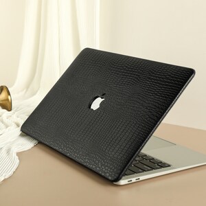 May include: Black laptop case with a crocodile-embossed texture. The case has a cut-out for the Apple logo.