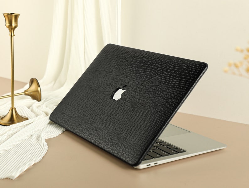 May include: Black laptop case with a crocodile-embossed texture. The case has a cut-out for the Apple logo.