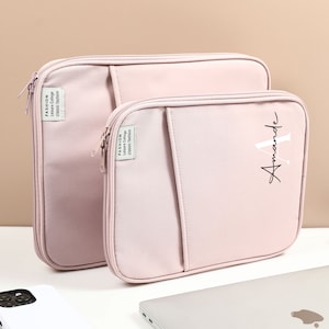 May include: Two pink laptop sleeves, one slightly larger than the other. The smaller sleeve has the name "Amanda" written on it in black cursive.