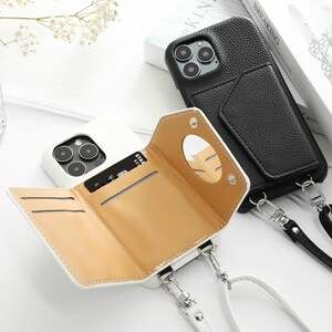 May include: Two white phone cases with a wallet and a strap. One case has a black leather exterior and the other has a tan leather interior. Both cases have a mirror on the back.