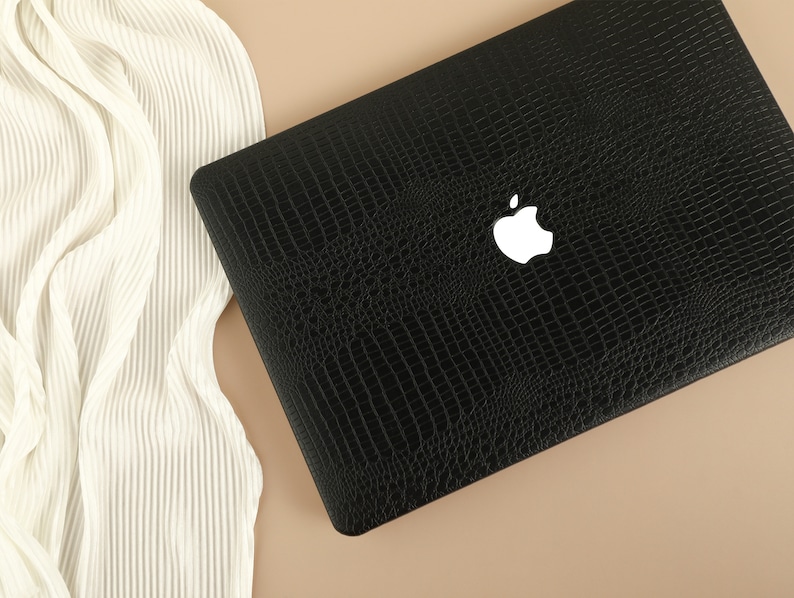 May include: A black laptop computer case with a crocodile skin pattern and a white Apple logo.