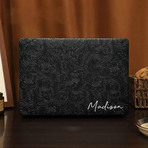 May include: Black laptop sleeve with a floral embossed pattern and the name "Madison" printed in white.