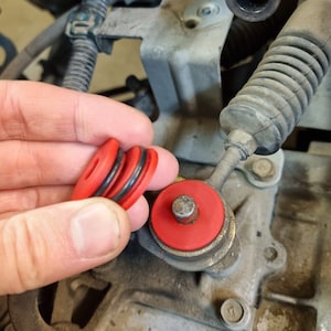 Puede incluir: Primer plano de tres arandelas de goma rojas y negras, dos se sostienen en una mano y una está instalada en una varilla de metal.