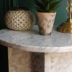 May include: A white marble round side table with a white and gold decorative candle holder and a small potted succulent plant.