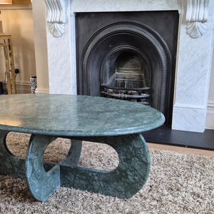 Peut inclure: Table basse ovale en marbre vert avec un design de base unique. La table est posée sur un tapis de couleur neutre dans un salon. La table mesure environ 122 cm de long et 61 cm de large.